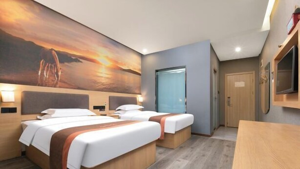 Habitació d'hotel amb dos llits, un quadre gran del capvespre, una taula de fusta i un televisor fixat a la paret.