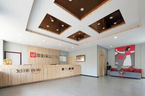A reception area with a wooden reception desk, a wall-mounted sign, and a seating area with a couch and chairs. - Junyi Hotel (Gucheng Railway Station Sanhuan Cheqiao Industrial Park) (Gucheng)