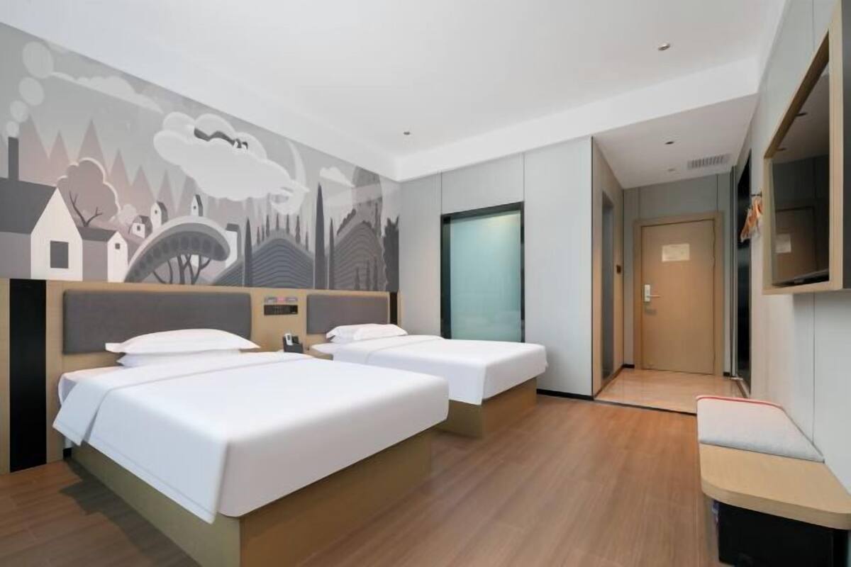 A hotel room with two beds, a TV, a mural on the wall, and a wooden floor.