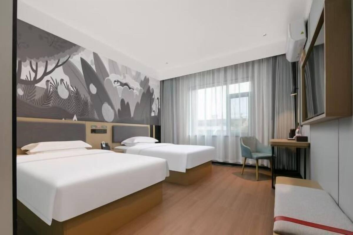A hotel room with two beds, a desk, a chair, and a large window with curtains.