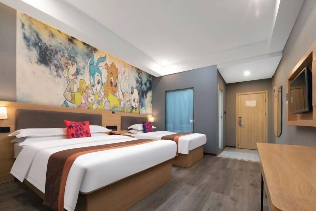 A hotel room with two beds, a large wall mural, a wooden desk, and a television.
