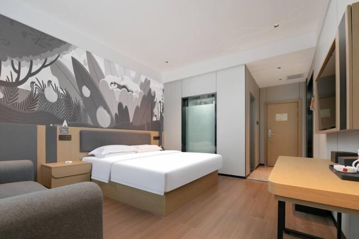 A modern hotel room with a bed, a desk, a chair, a TV, and a wall mural.