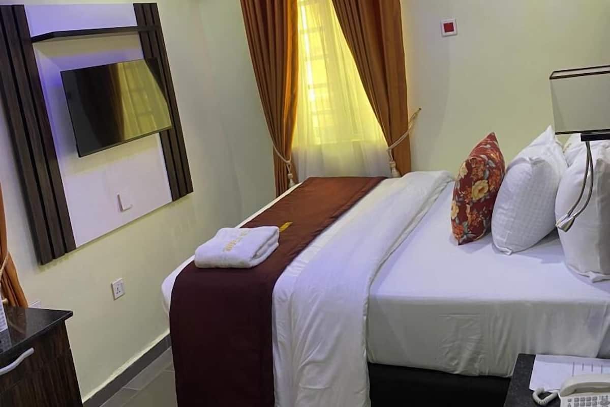 A hotel room with a bed, bedside table with a phone, a mirror, and a window with curtains.