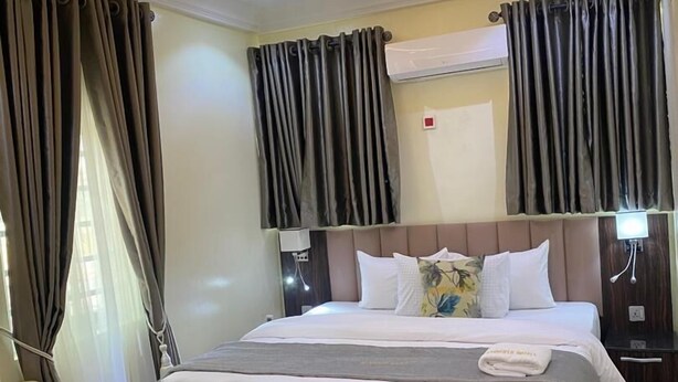 A hotel room with a large bed, a bedside table, a chair, and a modern ceiling design. - GrandField Hotels (Ibadan)