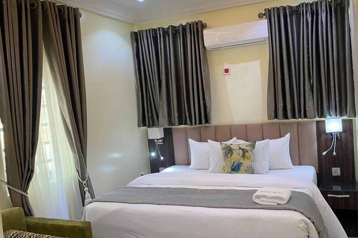 A hotel room with a large bed, a bedside table, a chair, and a modern ceiling design.