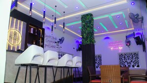 A bar area with white chairs, a bar counter, and a neon sign. - GrandField Hotels (Ibadan)