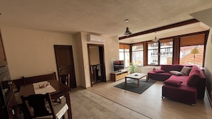 A living room with a dining area, a sofa, a TV, and large windows. - Charming Apartment City Escape (Brasov)