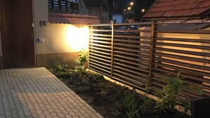 A paved patio area with a wooden fence, a door, and a small garden bed. - Charming Apartment City Escape (Brasov)