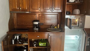 A compact kitchen with wooden cabinets, a coffee maker, a microwave, and a refrigerator. - Charming Apartment City Escape (Brasov)