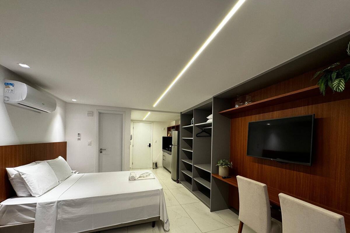 A modern hotel room with a bed, a TV, a wardrobe, and a seating area.
