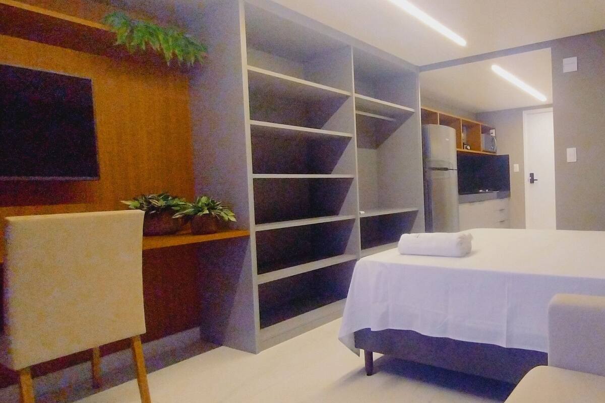 A bedroom with a bed, a sofa, built-in shelving, and a television.