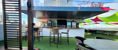 Un bar en la azotea con barra, zona de estar y vistas del horizonte urbano.