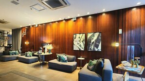 A modern lobby with wooden paneling, a seating area with sofas and armchairs, a small round table with a lamp, and a tray with decorative items. - Quality by Hosppedar (João Pessoa)