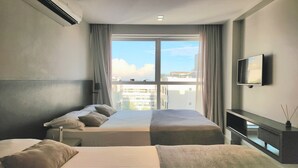A hotel room with a bed, a TV, and a view of buildings through the window. - Quality by Hosppedar (João Pessoa)