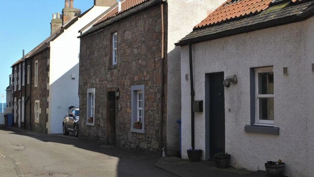 A row of traditional stone and plaster houses with pitched roofs, a narrow street, and a clear sky. - 2a Rose St- cosy coastal cottage Fife (Saint Monans)