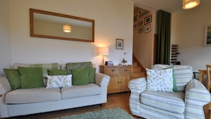 A living room with a sofa, armchair, and a wooden cabinet. - 2a Rose St- cosy coastal cottage Fife (Saint Monans)