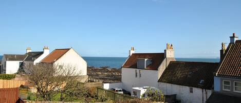 A coastal residential area with houses, a stone wall, and a view of the sea.