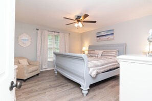 A bedroom with a bed, a chair, a ceiling fan, a window with curtains, and a painting on the wall. - Life's Been Good Beach House (Rehoboth Beach)