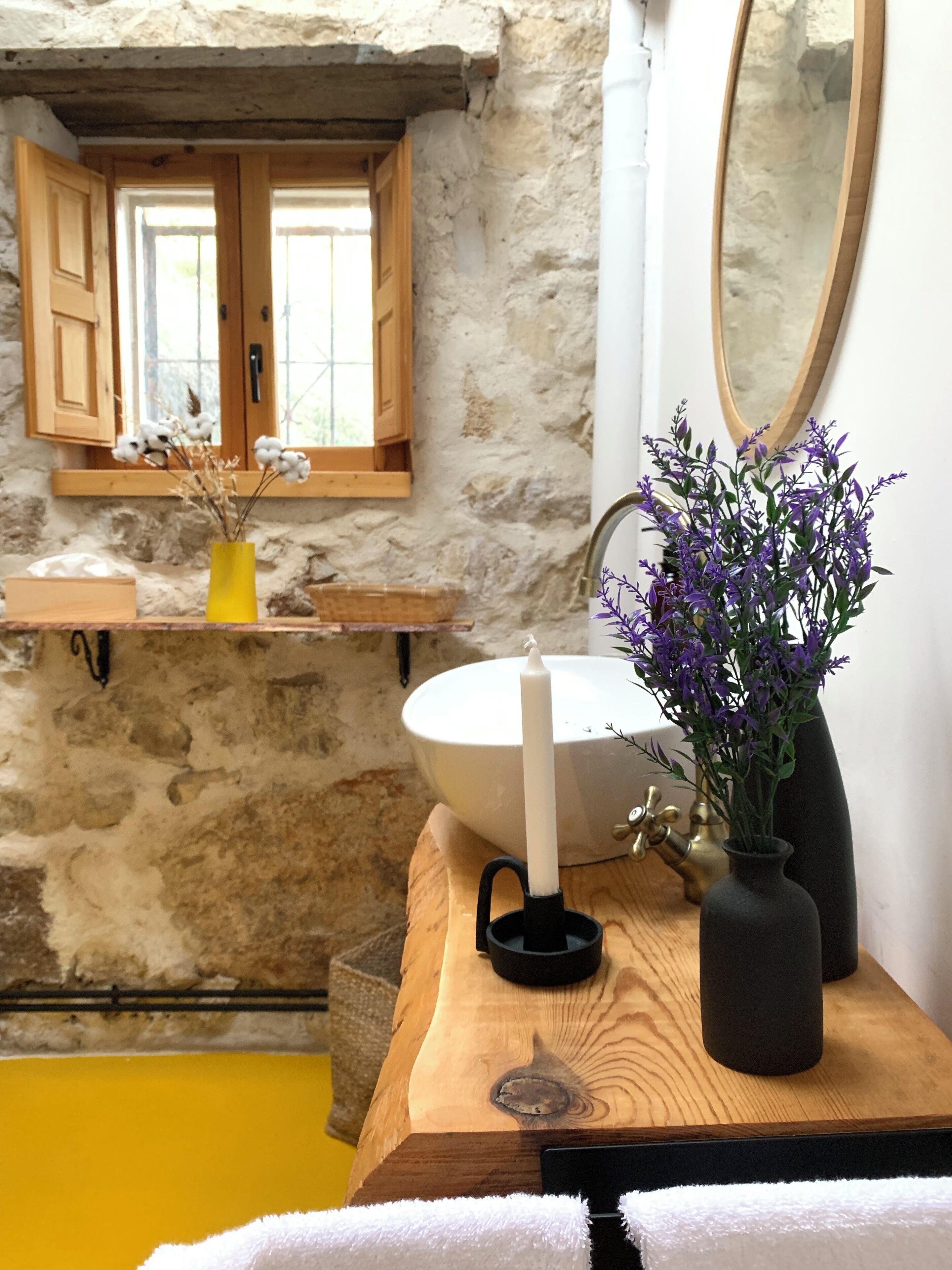 Un baño con pared de piedra, tocador de madera, lavabo blanco y un espejo.