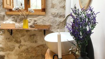 Un baño con pared de piedra, tocador de madera, lavabo blanco y un espejo.