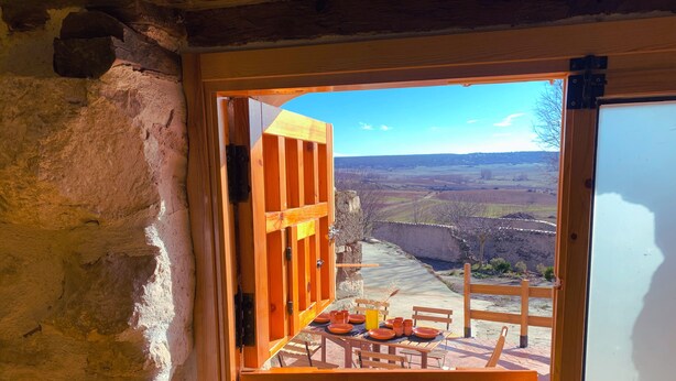Eine offene Holztür führt auf eine Terrasse mit Esstisch, mit Blick auf eine reizvolle Landschaft.