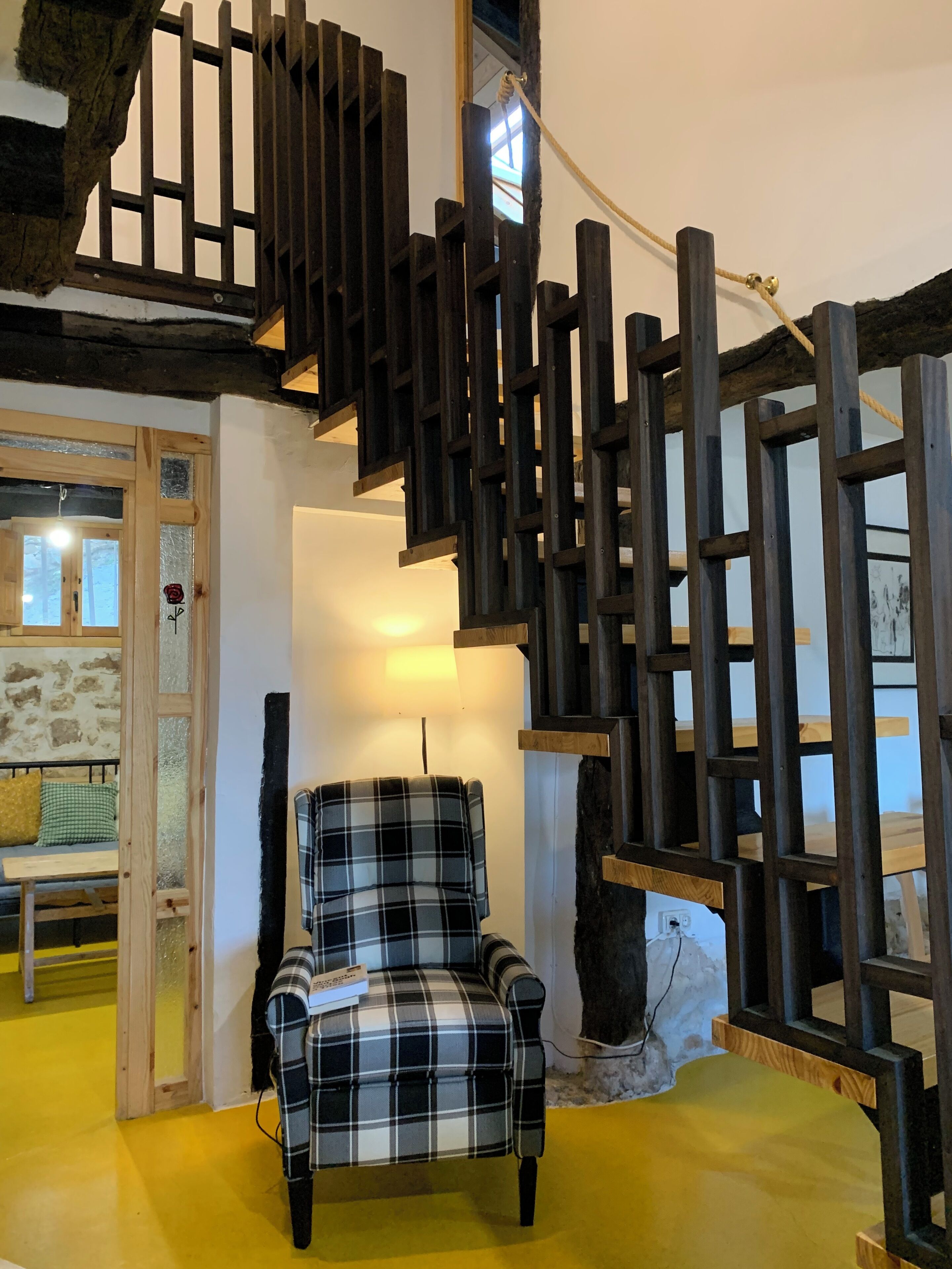 Una habitación con una escalera de madera, un sillón escocés y una pared de piedra.