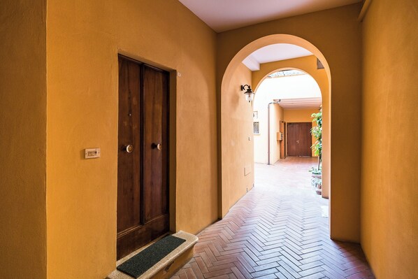 A corridor with a herringbone tile floor, wooden doors, and an arched doorway leading to another room. - Cozy central apartment by Wonderful Italy (Bologna)
