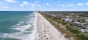 An aerial view of a beach with houses along the shore, a clear sky, and the ocean.