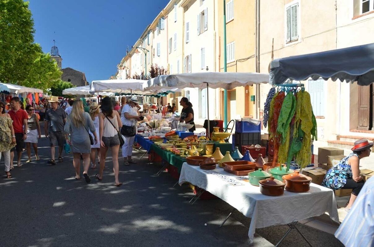 A bustling outdoor market with tables displaying various goods, surrounded by buildings.