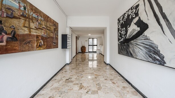 A hallway with a marble floor, a large mural on the left, and a black and white painting on the right. - Mutina Suite 3 (Modena)