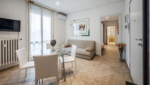 A modern living room with a glass table, white chairs, a beige sofa, and a flat-screen TV mounted on the wall. - Mutina Suite 3 (Modena)