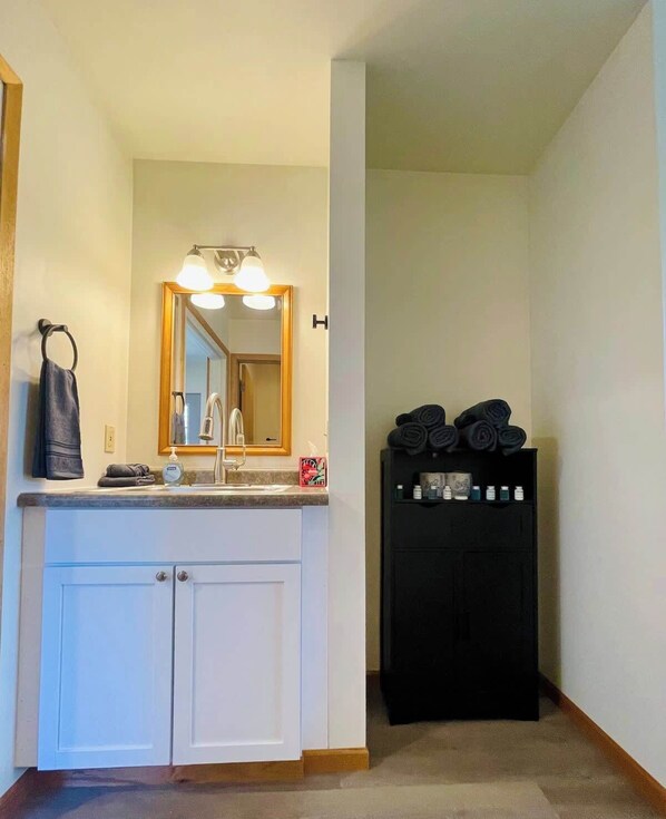A bathroom with a sink, mirror, towel rack, and a black cabinet with toiletries. - Renovated Two-Story Apartment Near Wisconsin Dells Attractions (Wisconsin Dells)