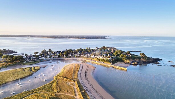 Vista aérea de un pueblo costero con un puerto deportivo, playas de arena y edificios residenciales.