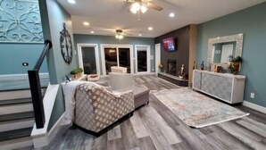 A spacious living room with a grey patterned sofa, a fireplace, and a decorative mirror. - 17 ft Swim Spa, hot tub, pool table, kayaks, 3 kitchens, wifi (Moneta)