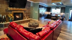 A living room with a red leather sofa, a fireplace, and a kitchen in the background. - 17 ft Swim Spa, hot tub, pool table, kayaks, 3 kitchens, wifi (Moneta)
