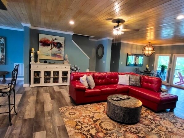 A living room with a red sectional sofa, a patterned rug, a round coffee table, and a white cabinet with glass doors. - 17 ft Swim Spa, hot tub, pool table, kayaks, 3 kitchens, wifi (Moneta)