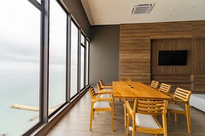 A modern dining area with a large wooden table and chairs, a flat-screen TV mounted on a wooden panel wall, and a view of the sea through large windows. - U-GO Vistas al Mar desde Murano Centro (Cartagena)