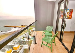 A balcony with a view of the beach and ocean, a green chair, and a glass door leading to an interior space. - U-GO Vistas al Mar desde Murano Centro (Cartagena)