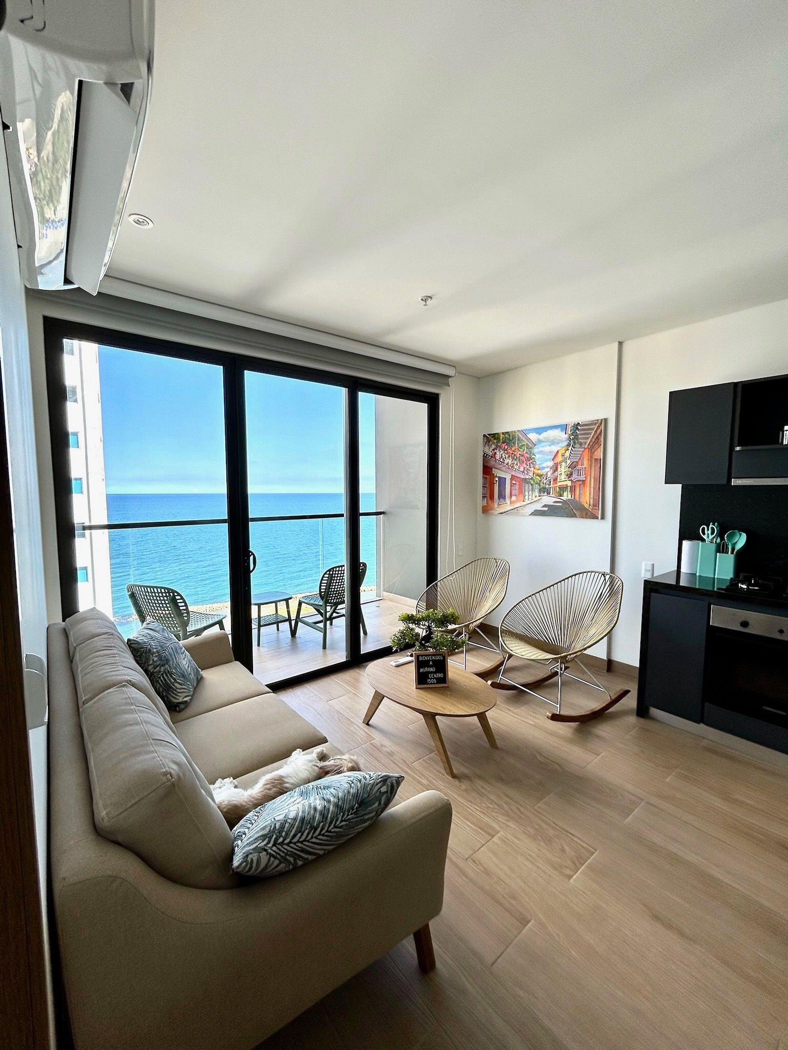 A modern living room with a sofa, chairs, a coffee table, and a view of the sea through large windows.