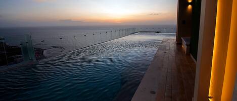 An infinity pool with a view of the ocean at sunset.