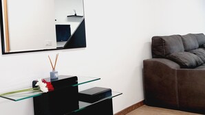 Un salon moderne avec un grand miroir, une table basse en verre, un canapé foncé et une petite table d’appoint noire agrémentée d’un vase et de bougies.