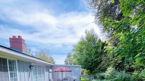 Un jardin avec une terrasse, un parasol rouge et une maison avec une cheminée.