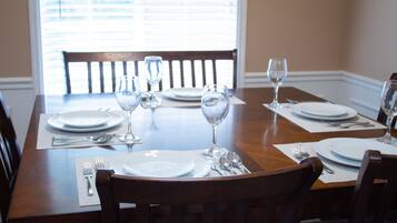 A dining table set with plates, cutlery, and wine glasses, with a window in the background.