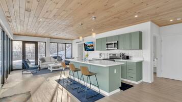 Una cocina moderna con una isla central, armarios verdes y un amplio ventanal con vistas a un paisaje nevado.