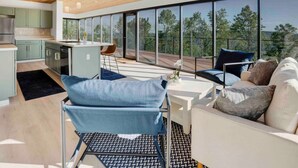 A modern living space with a kitchen, dining area, and seating by large windows overlooking a forest. - Breathtaking views, modern container design (Little Valley)