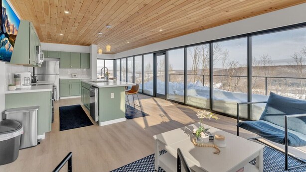 A modern kitchen with large windows, a dining area, and a view of a snowy landscape. - Breathtaking views, modern container design (Little Valley)