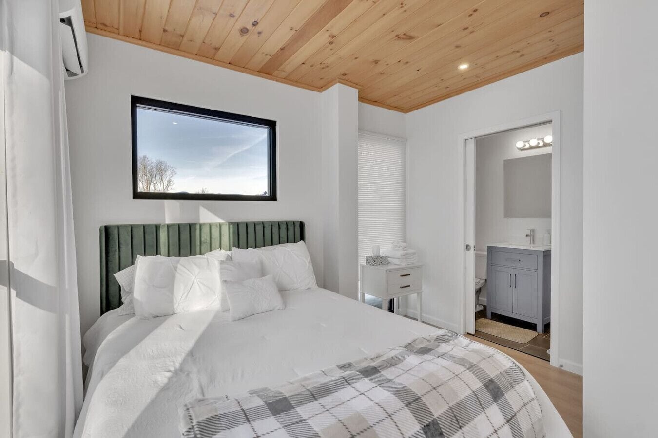 A bedroom with a bed, a window, a mirror, and a bathroom visible through an open door.