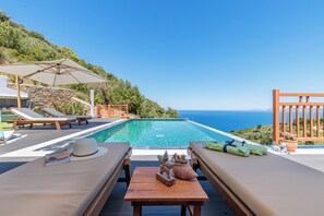 A poolside area with lounge chairs, a table with a hat and a book, and a view of the sea.