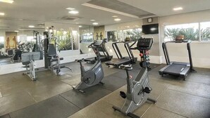Et fitnesscenter med diverse træningsmaskiner, et stort spejl og en tv-skærm.