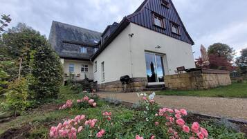 Ein zweistöckiges Haus mit einem steilen Walmdach, einem Steinfundament und einer Veranda mit einer Bank.